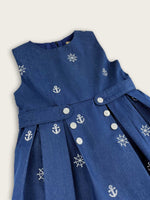 Blue nautical denim girls dress featuring white embroidered anchor and ships wheel motifs close up view with buttons