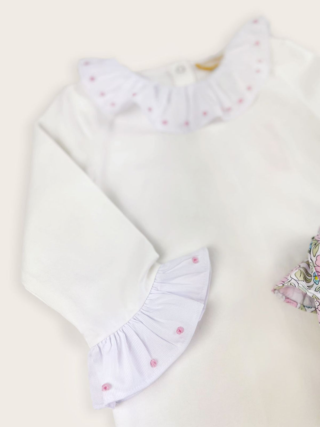 Pink dots embroidered onto the frilled collar and cuffs of a white bodysuit paired with floral bloomers.